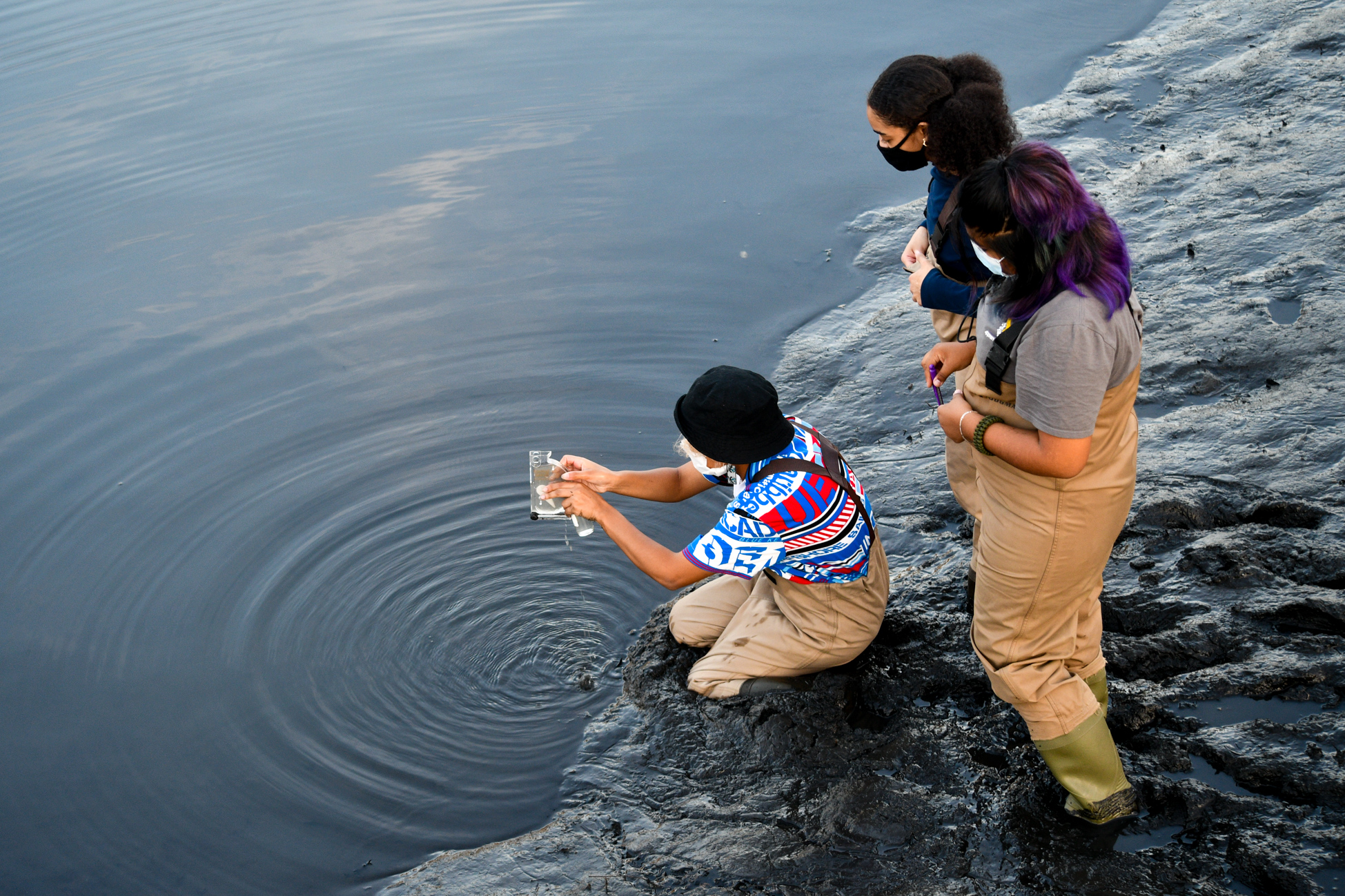 Students test water quality while wearing masks and waders